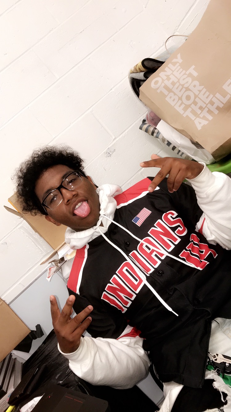 Miggy posing while sitting down,throwing up signs with his hands, along with sticking his tongue out.